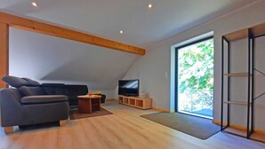 Una sala de estar moderna con un sofá, una televisión y un ventanal amplio.