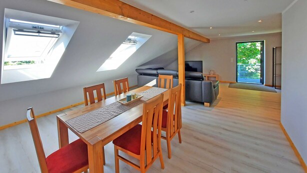 Un comedor con una mesa y sillas de madera, un sofá y un televisor en un espacio habitable moderno con tragaluces.