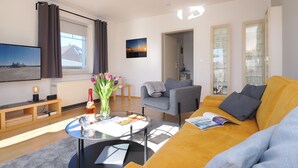 A modern living room with a sofa, a coffee table, a TV, and a glass cabinet. - Fewo Sonnenblick - Fewo Sonnenblick (Heringsdorf)