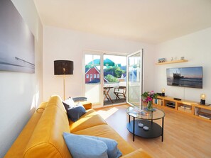 Ein modernes Wohnzimmer mit Sofa, Couchtisch, Fernseher und einem Balkon mit Blick auf Häuser und Grünflächen.