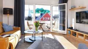A modern living room with a sofa, a coffee table, a TV, and a balcony with a view of a red house. - Fewo Sonnenblick - Fewo Sonnenblick (Heringsdorf)
