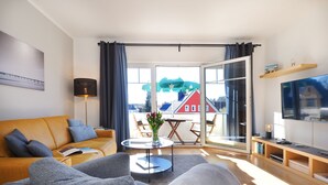 A living room with a sofa, armchairs, a coffee table, a TV, and a balcony with a view of houses. - Fewo Sonnenblick - Fewo Sonnenblick (Heringsdorf)