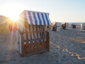 Ein Liegestuhl mit gestreiftem Sonnendach, Holzrahmen und gepolstertem Sitz.