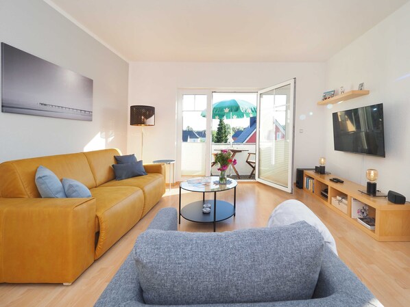 Ein modernes Wohnzimmer mit einer Couch, einem Couchtisch, einem Fernseher und einem Balkon mit Blick.
