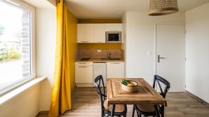 Una cocina compacta con armarios blancos, microondas y lavamanos. Hay una mesa de comedor con sillas y una cesta de fruta.