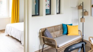 Una habitación moderna con cama, sofá de mimbre con cojines, una mesita y una lámpara de pie.
