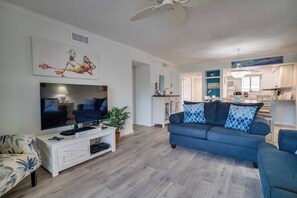 En moderne stue med et fladskærms-tv, en sofa og et spiseområde med en lysekrone.
