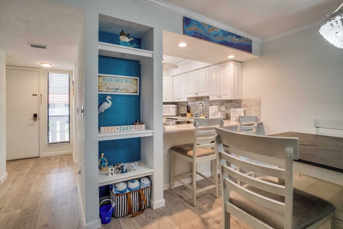 A modern kitchen with white cabinets, a dining area with a wooden table and chairs, and a blue accent wall with decorative items.