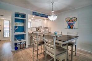 A dining area with a wooden table and white chairs, a chandelier, and a blue wall with decorative items.