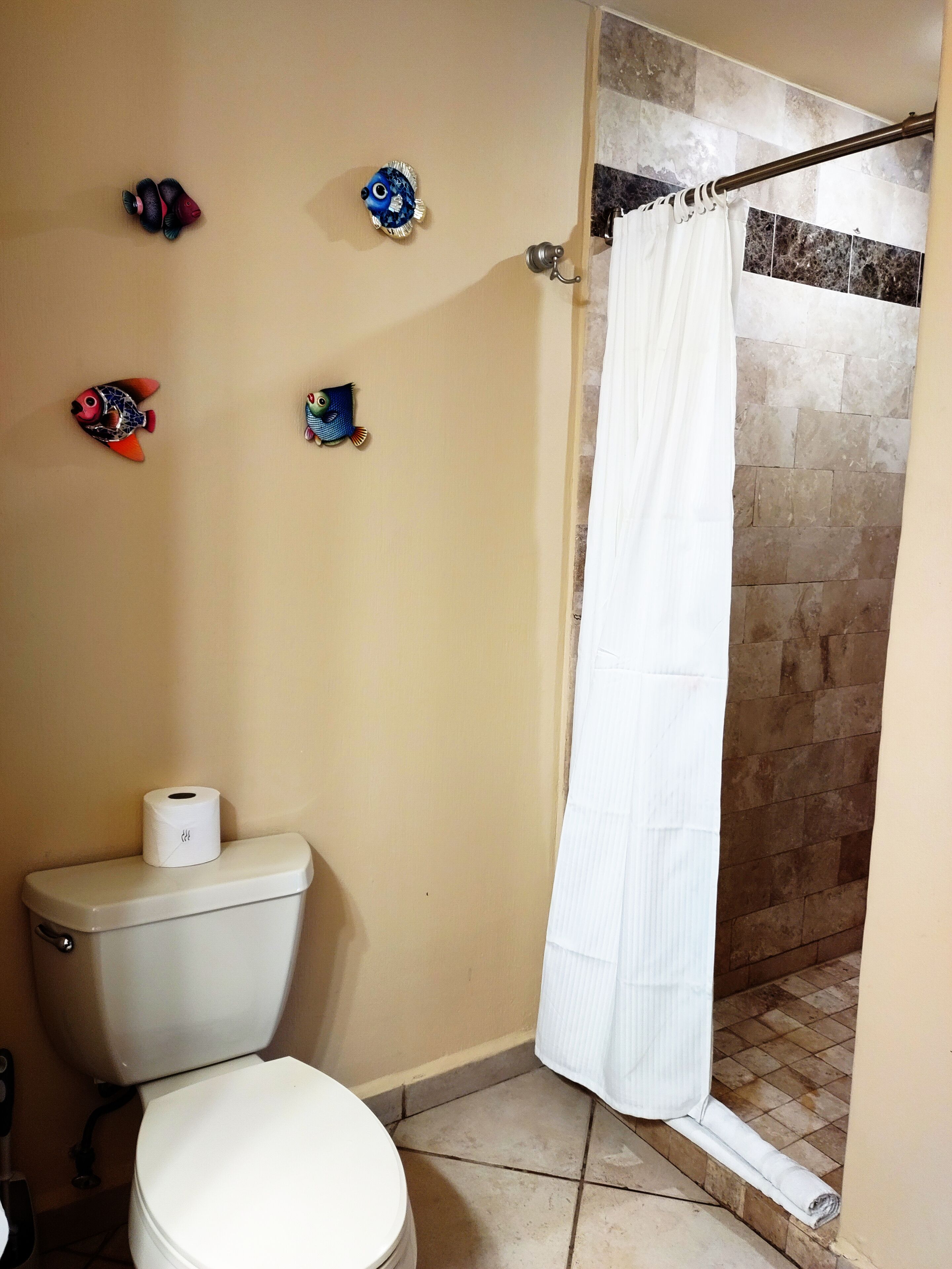 Une salle de bain avec des toilettes, un rideau de douche et des décorations murales représentant des poissons.