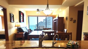 A kitchen with a double sink, dining table, chairs, and a view of the ocean through large windows.