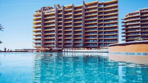 A multi-story hotel with balconies, a swimming pool, and a clear blue sky.