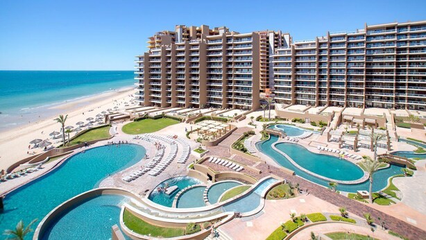 A hotel with multiple swimming pools, a beach, and a large building with balconies.