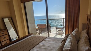 A bedroom with a large bed, a view of the ocean, and a balcony with outdoor furniture.