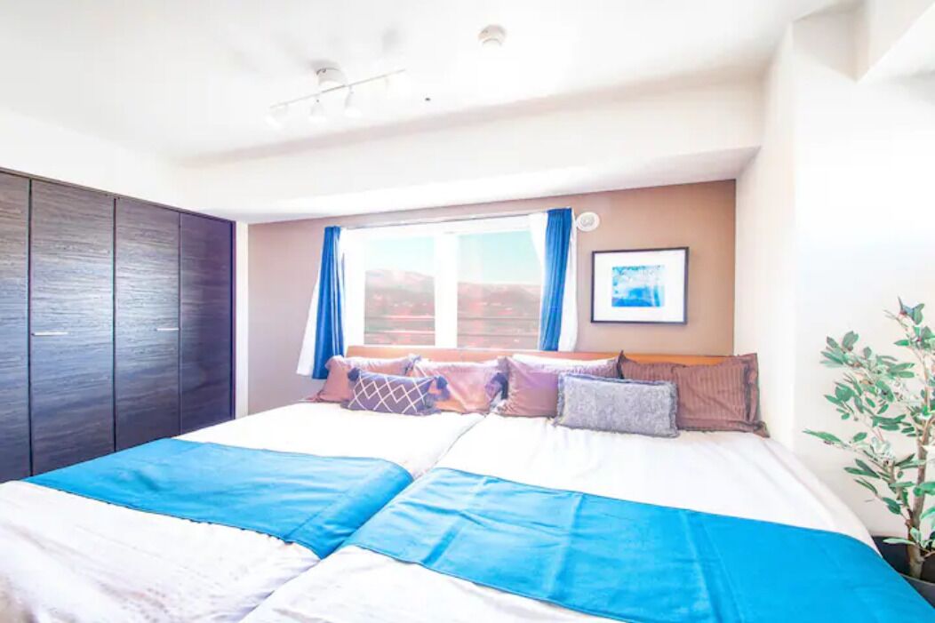 A bedroom with a large bed, a wardrobe, a window with curtains, and a framed picture on the wall.