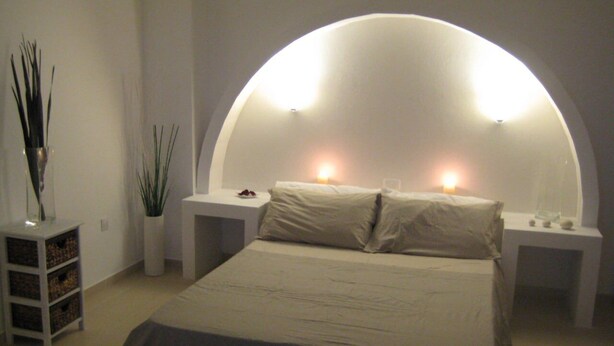 Un dormitori modern amb un llit gran, dues taules de nit, una làmpada de paret i una petita planta.
