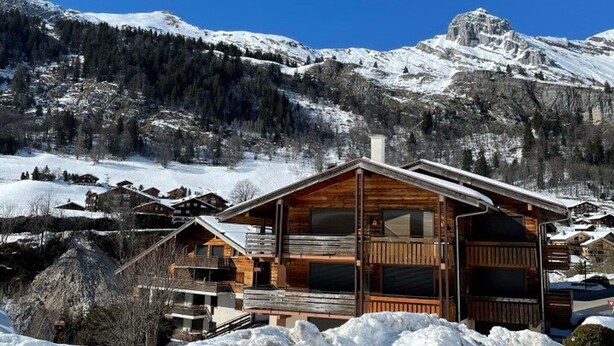 A wooden cabin with a balcony, surrounded by snow-covered mountains and trees.