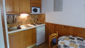 A compact kitchen with wooden cabinets, a microwave, a sink, and a small refrigerator.
