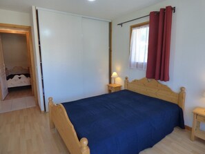 Un dormitorio con una cama de madera, una mesita de noche, un armario y una ventana con cortinas.