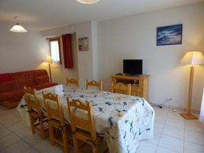 Una habitación con una mesa de comedor, sillas, un televisor sobre un soporte de madera, un sofá y una lámpara.