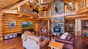 Interior de una cabaña de troncos con chimenea, muebles de madera y televisor.