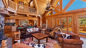 A spacious log cabin interior with a pool table, leather sofas, and a fireplace.