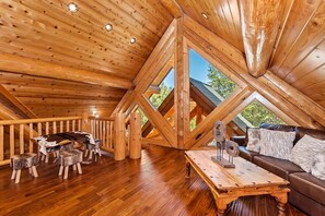 A wooden interior with a dining table and chairs, a sofa, and a fireplace. - Luxury 5 Bedroom! Custom Log Home! A/C! Hot Tub! Pool Table! Foosball! BBQ! (Big Bear City)