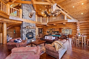 A spacious log cabin interior with a fireplace, multiple seating areas, and a pool table.