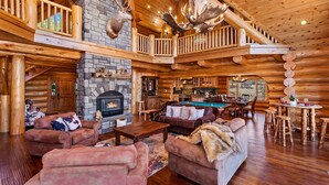 A log cabin interior with a stone fireplace, a pool table, and a cozy seating area.