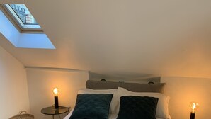 A neatly made bed with white linens and a rolled towel, two dark pillows, and two bedside lamps on small tables. - Simply Pinoche Room Proche Plage (Saint-Malo)