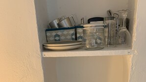 A kitchen with a kettle, coffee maker, and various kitchenware on shelves. - Simply Pinoche Room Proche Plage (Saint-Malo)