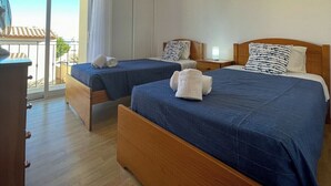 Habitación de hotel con dos camas, un aparador de madera y un balcón con vistas a la ciudad.
