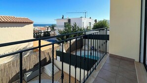 Un balcón con piscina, vista al mar y un paisaje urbano al fondo.
