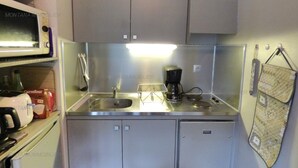 Une petite cuisine équipée, avec des appareils en acier inoxydable, notamment un four à micro-ondes, une machine à café et un évier.