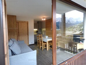 Ein modernes Interieur mit einer Couch, einem Esstisch und Stühlen, und einem großen Fenster mit Blick auf die Berge.