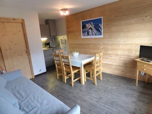 Un espacio habitable compacto con comedor, kitchenette y televisor sobre un soporte de madera.