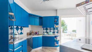 A modern kitchen with blue cabinets, a white countertop, and a view to the outdoor dining area. - VILLA NICE-GAIRAUT VI4230 BY RIVIERA HOLIDAY HOMES (Niza)