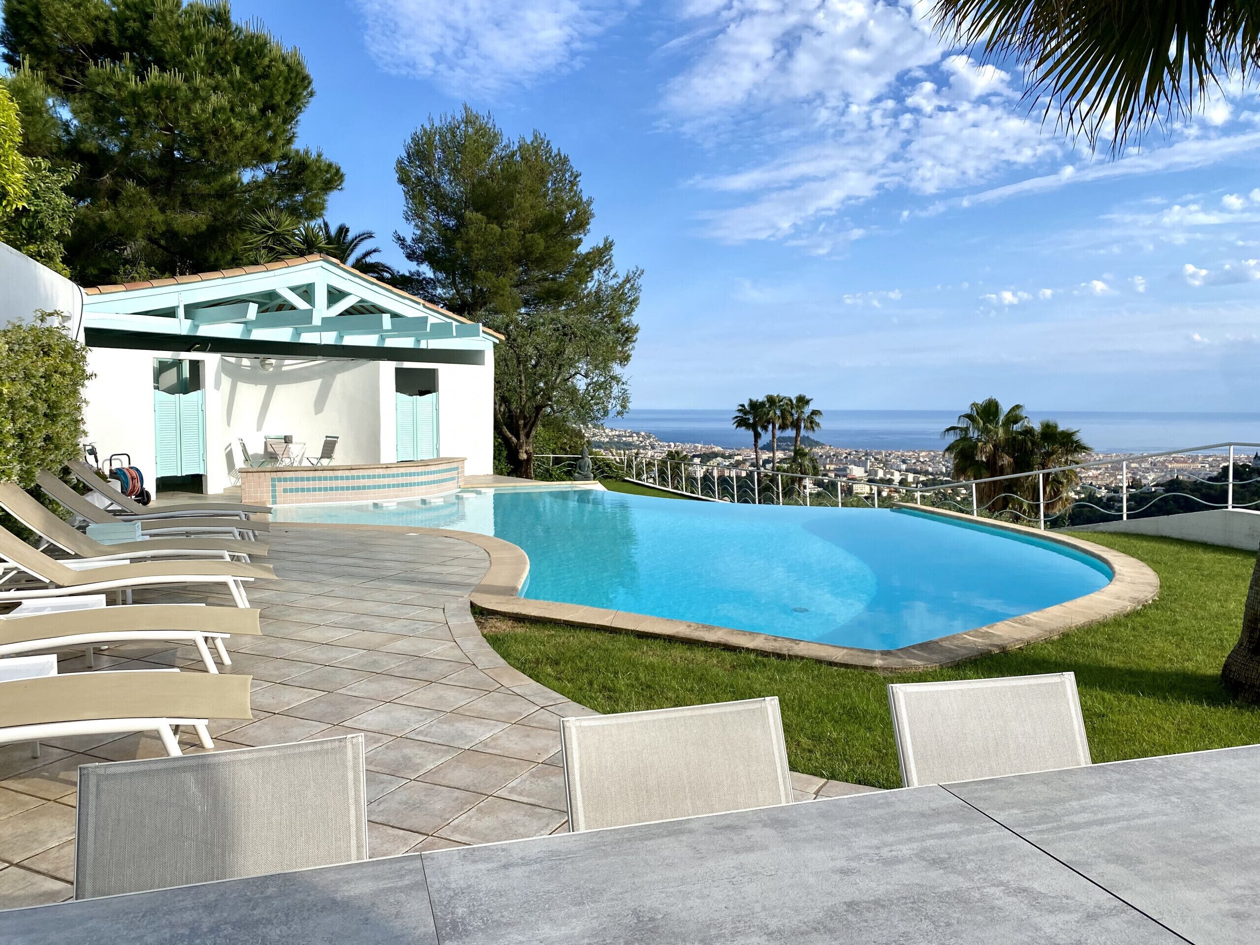 Una piscina con lettini, un piccolo edificio con tetto blu e vista sull'oceano.
