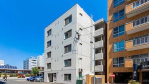A multi-story building with a white facade, a visible fire escape, and a storefront with a sign. - Green (Sapporo)