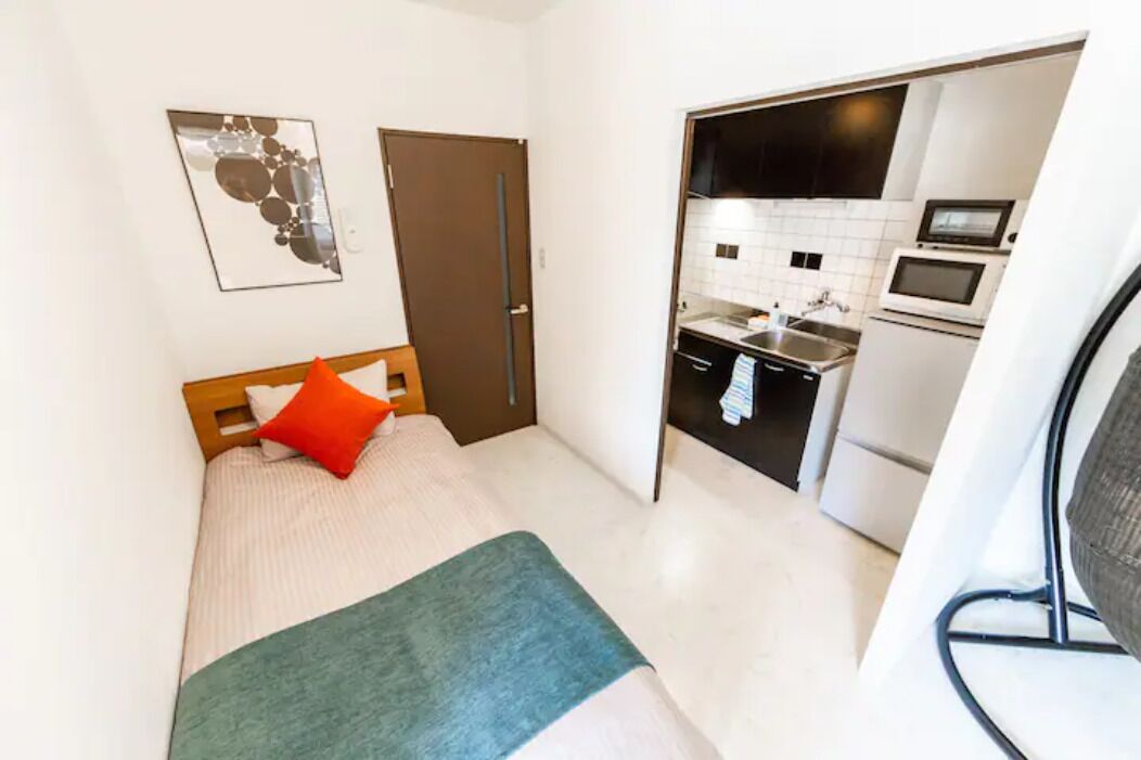 Un dormitorio pequeño con cama, una puerta y una kitchenette en la habitación contigua.