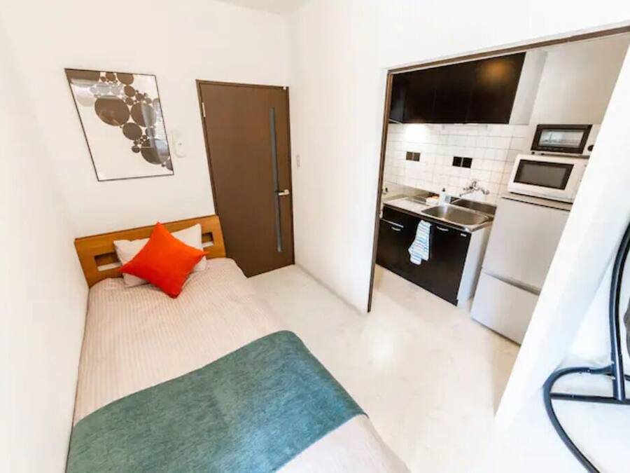 Un dormitorio pequeño con cama, una puerta y una kitchenette en la habitación contigua.