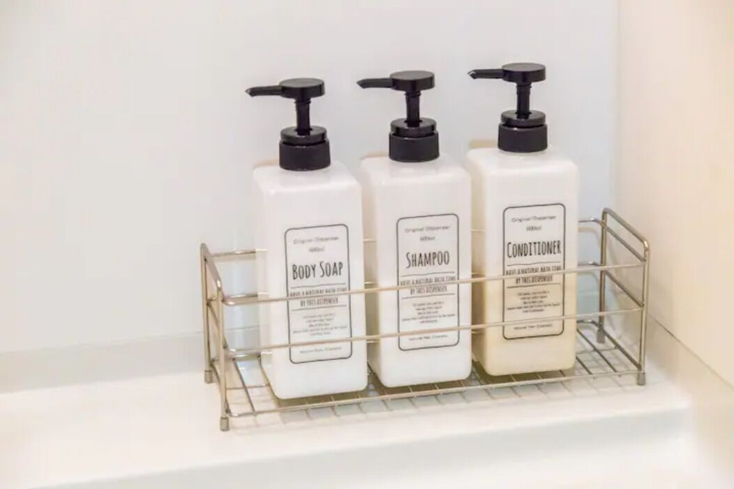 Three bottles of body soap, shampoo, and conditioner on a metal shelf.
