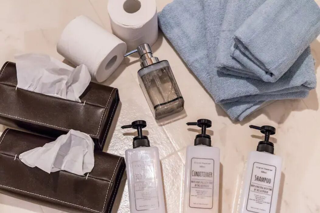 Toiletries including body wash, conditioner, and shampoo, along with a towel and toilet paper on a beige surface.