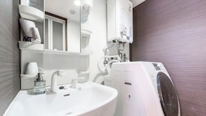 A modern bathroom with a white sink, a mirror, a towel rack, and a built-in washing machine. - Green (Sapporo)