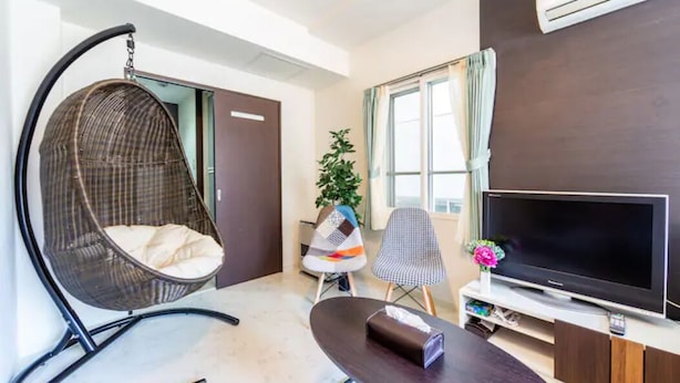 A modern living room with a large flat-screen TV, a hanging chair, a small table, and a potted plant. - Green (Sapporo)