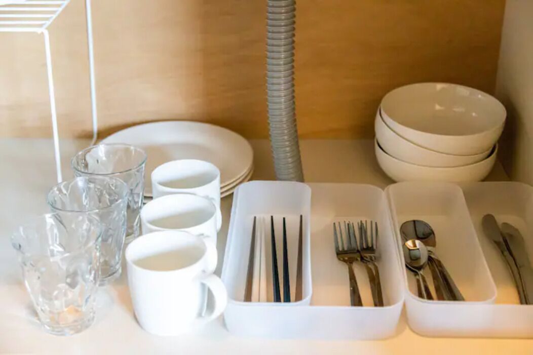 A neatly arranged table with white mugs, glasses, plates, and cutlery in white containers.