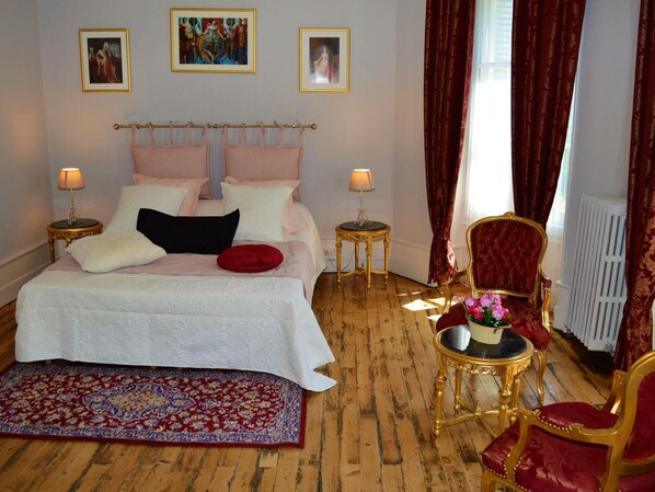 A bedroom with a large bed, two bedside tables, a red chair, and a small table with flowers.