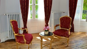 A room with two ornate chairs, a small table with a vase of flowers, and a radiator.