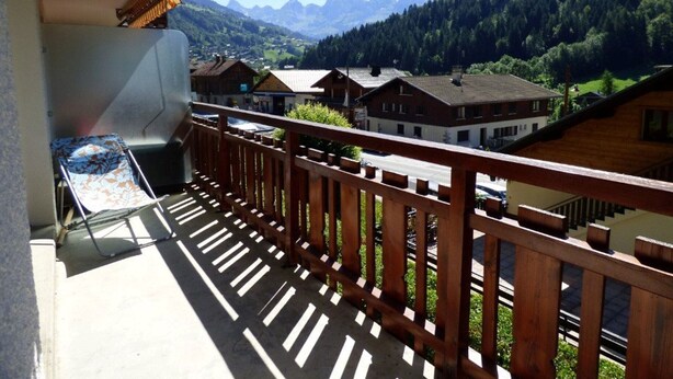 En balkon med udsigt til et bjerglandskab, en stol og et bord.