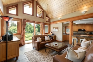 A spacious living room with a leather sofa, a glass coffee table, and a view of the outdoors through large windows.